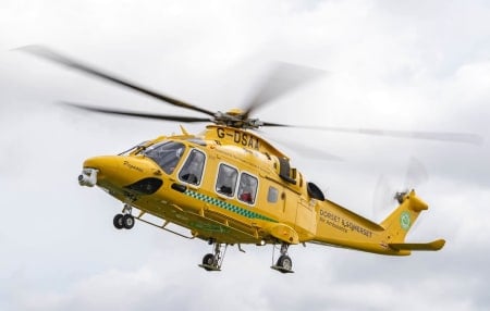 an image of dorset and somerset air ambulance helicopter flying in the sky on a cloud day