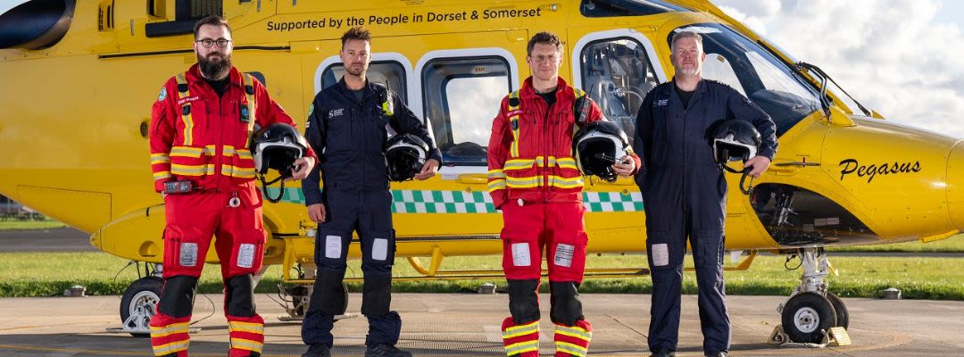 Four members of the Dorset and Somerset Air Ambulance Crew in front of the yellow Helicopter